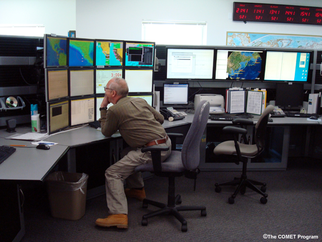 A man looks at a bank of 16 monitors at the Alaska and West Coast Tsunami Warning Center